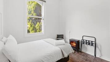 Une chambre à coucher avec un lit, une fenêtre, un téléviseur et un poêle à bois.