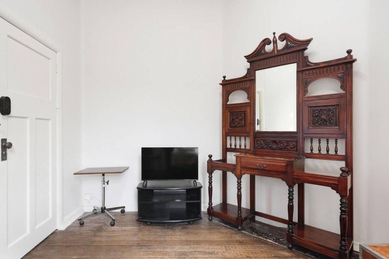 A room with a white door, a black entertainment unit, and a wooden dresser with a mirror.