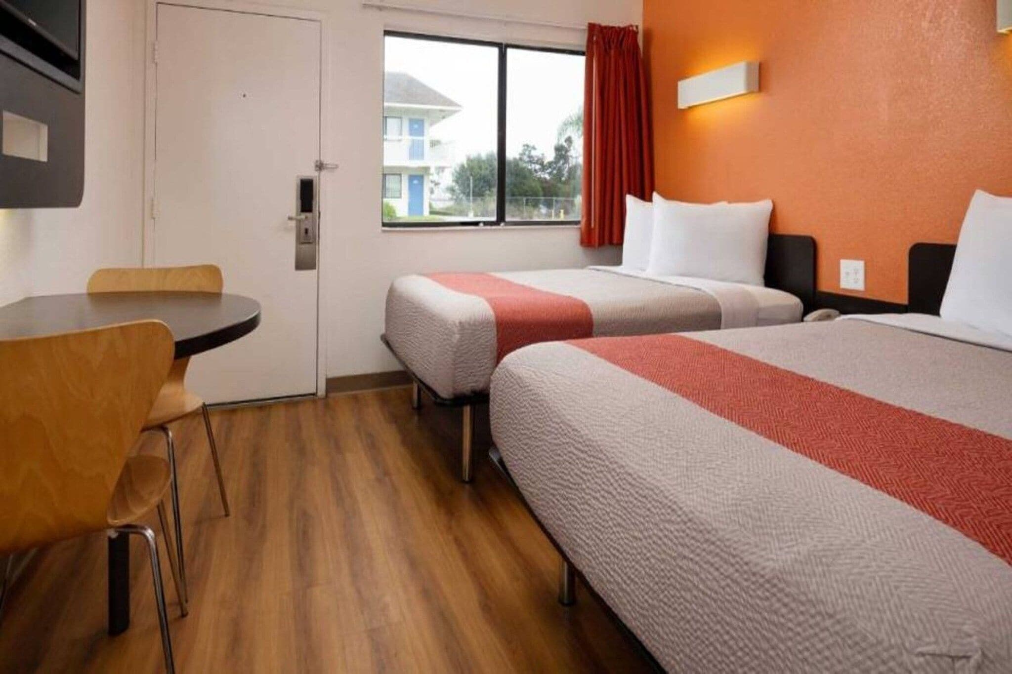 A hotel room with two beds, a small table, and a chair.