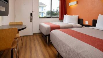 A hotel room with two beds, a small table, and a chair.