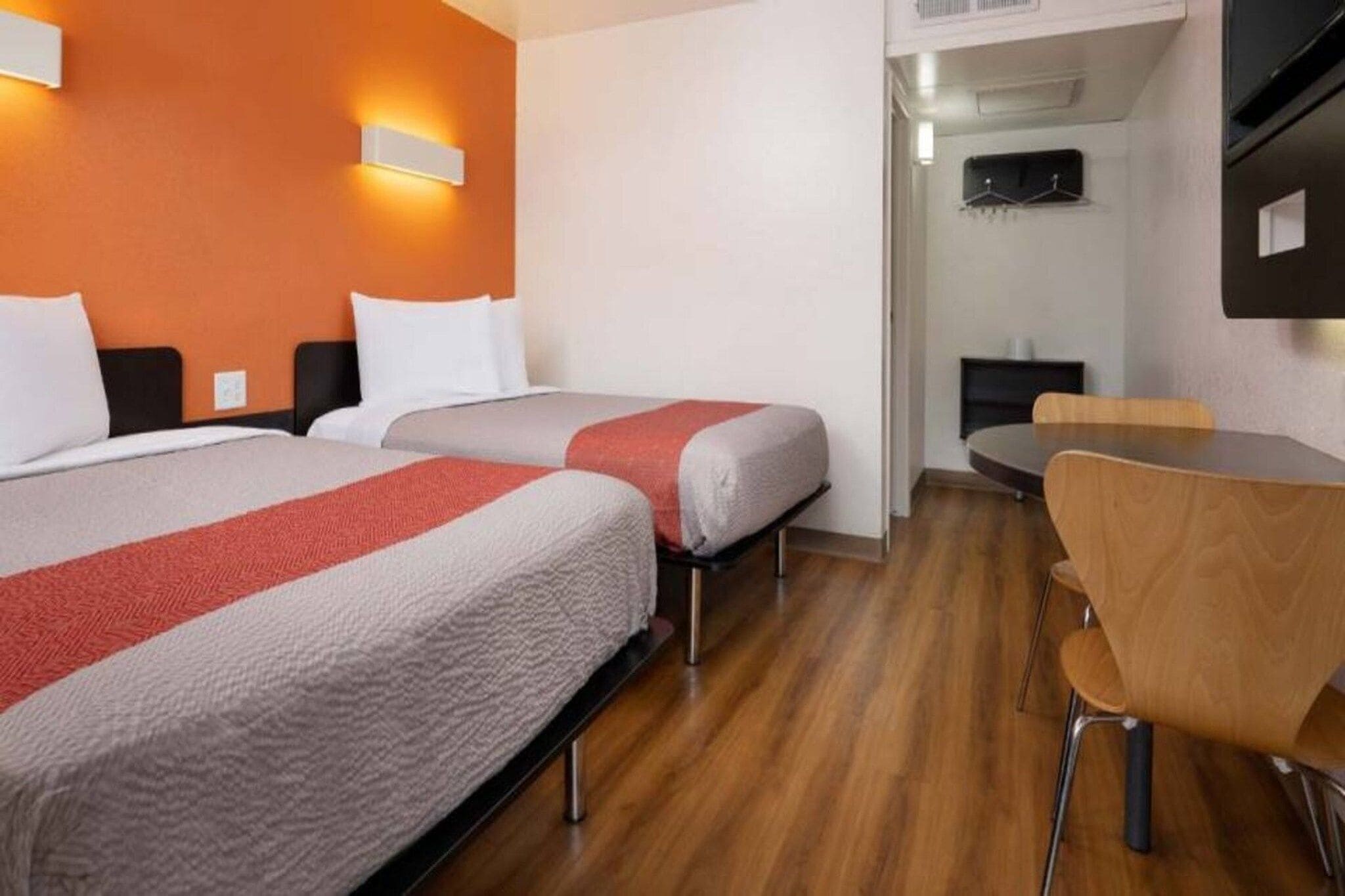 A hotel room with two beds, a dining table, and a TV mounted on the wall.