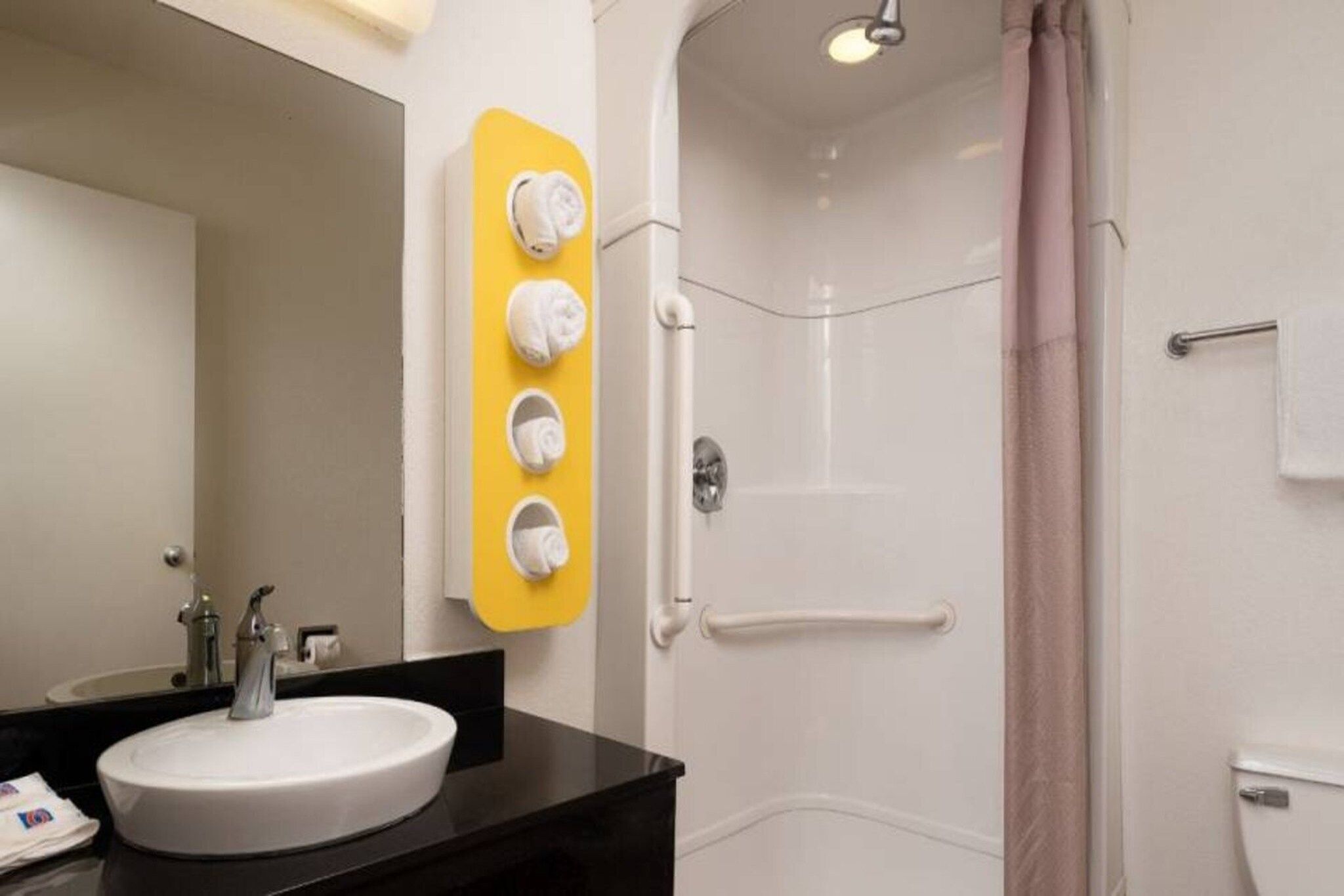 A bathroom with a white sink, a mirror, a shower with a glass door, and a towel rack with four white towels.