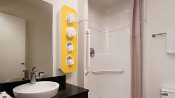 A bathroom with a white sink, a mirror, a shower with a glass door, and a towel rack with four white towels.