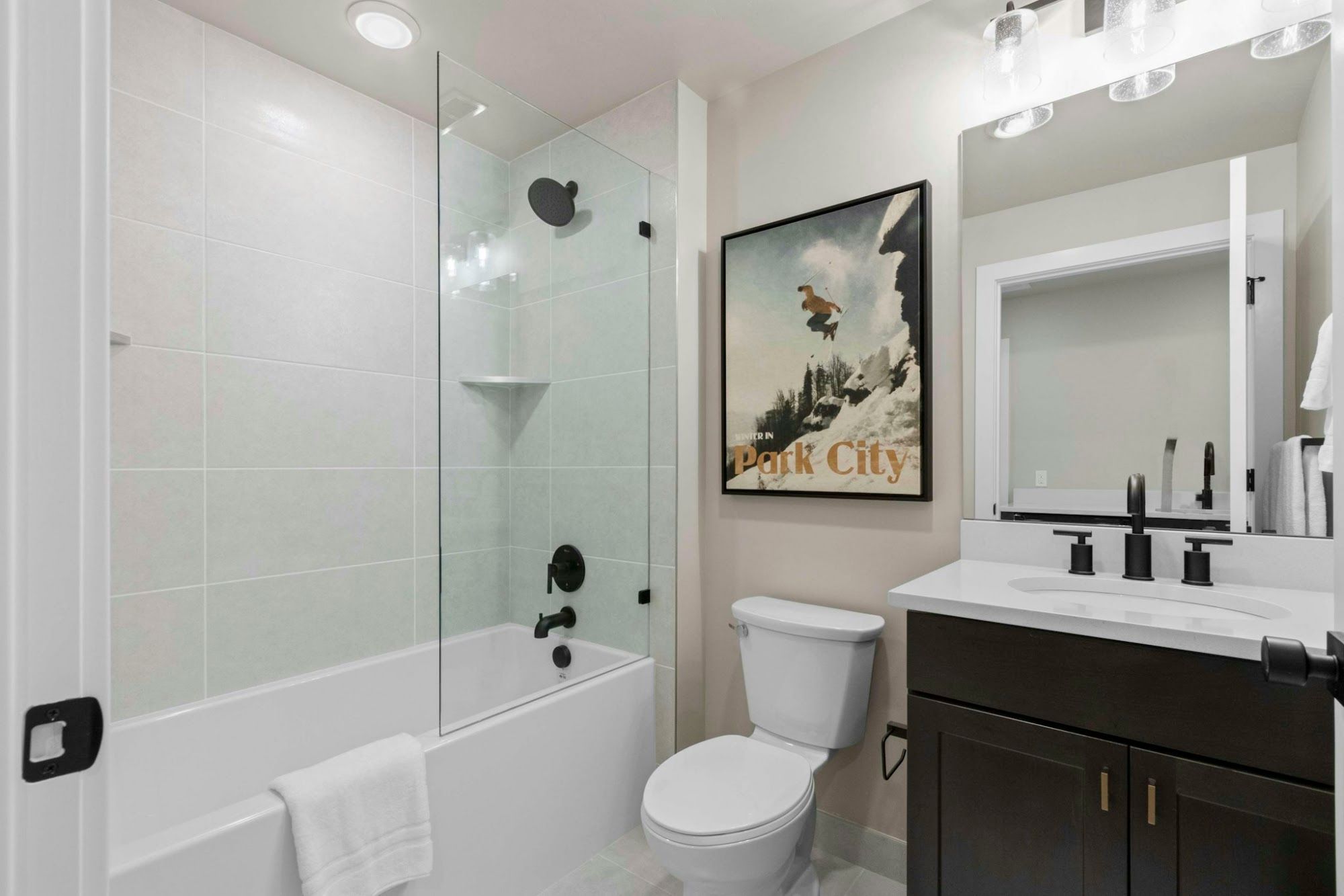 A bathroom with a glass-enclosed shower, a white toilet, a sink with a mirror, and a framed picture on the wall.