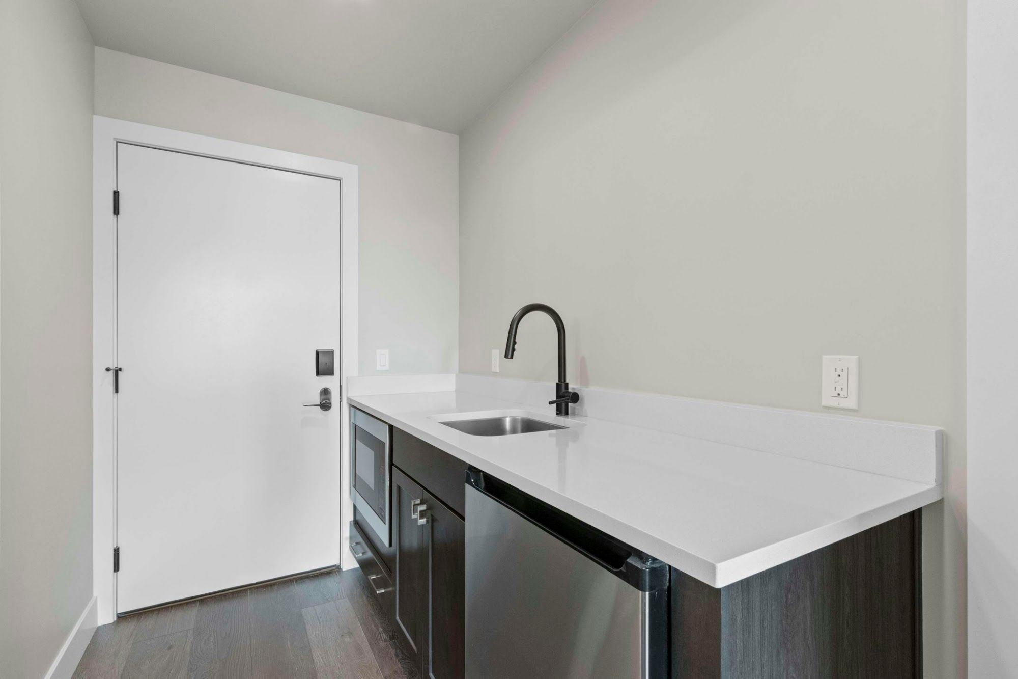 A compact kitchen with a white countertop, a stainless steel sink, and a door with a handle.