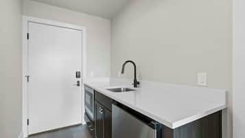 A compact kitchen with a white countertop, a stainless steel sink, and a door with a handle.