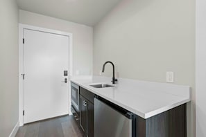 A compact kitchen with a white countertop, a stainless steel sink, and a door with a handle. - King Guest Room with Wet Bar | Pet-Friendly (Heber City)