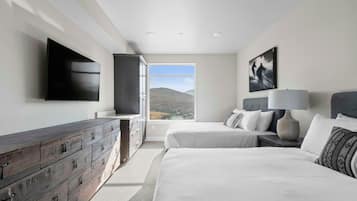 A bedroom with a bed, a dresser, a TV, and a window with a view of hills.