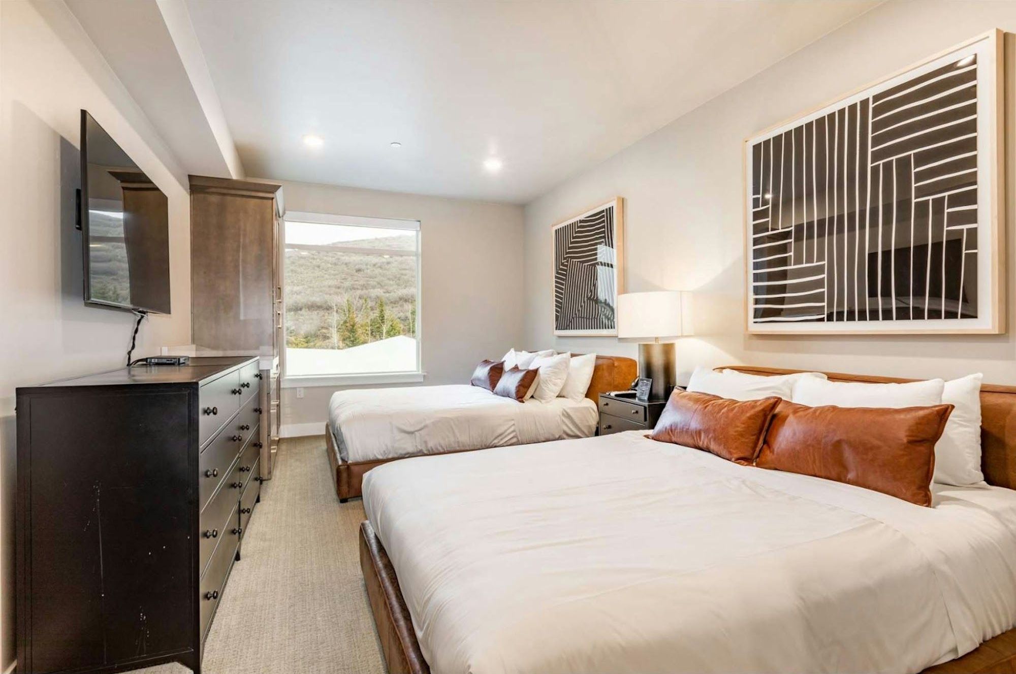 Two queen beds with leather headboards and mountain hillside view through window