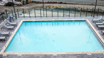 A rectangular swimming pool with a tiled edge, surrounded by lounge chairs and a metal fence.