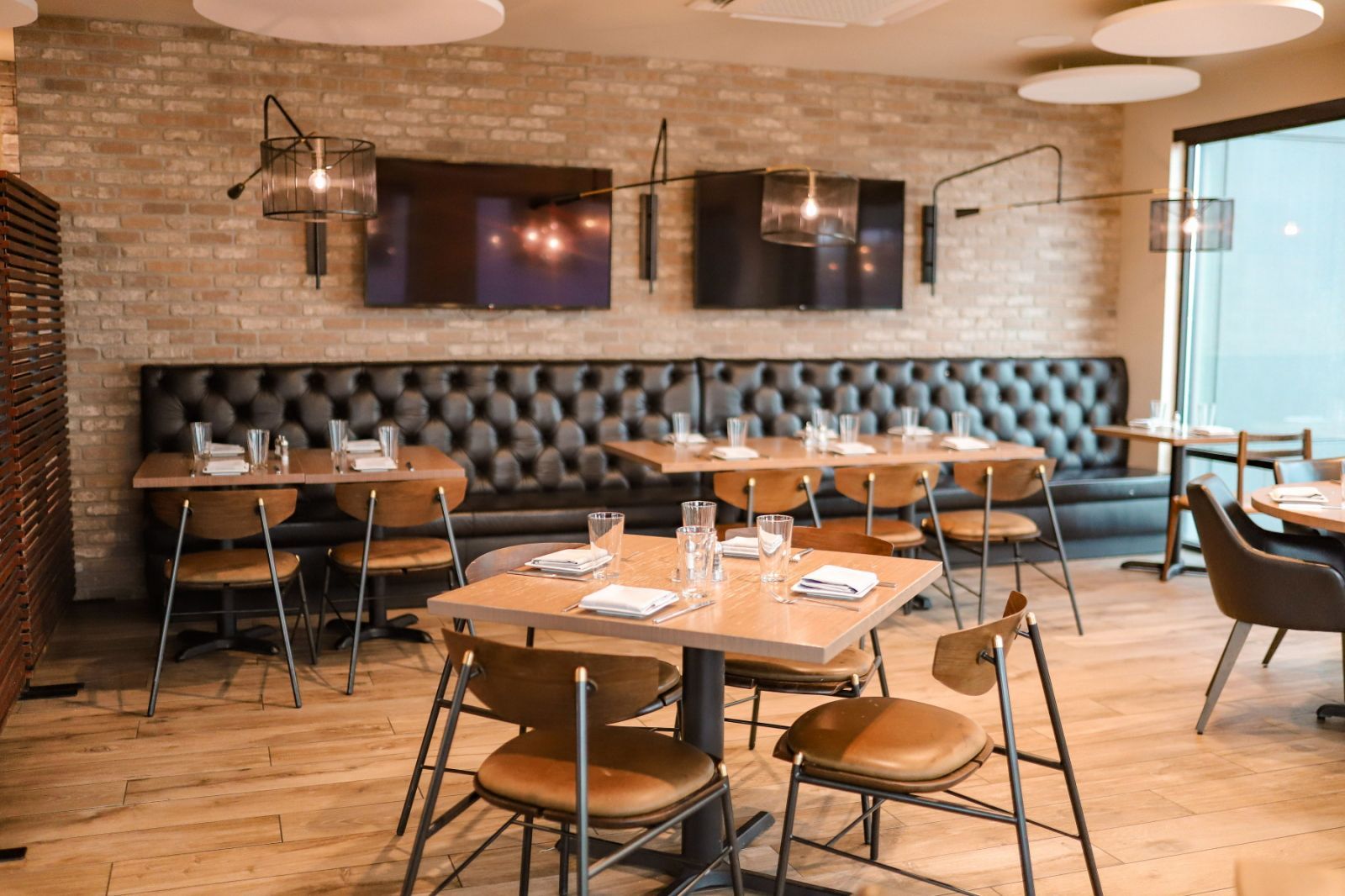 A restaurant interior with brick walls, cushioned seating, and modern lighting fixtures.