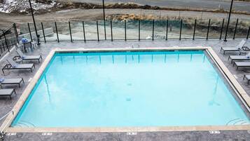 A rectangular swimming pool with a tiled deck, surrounded by lounge chairs and a metal fence.