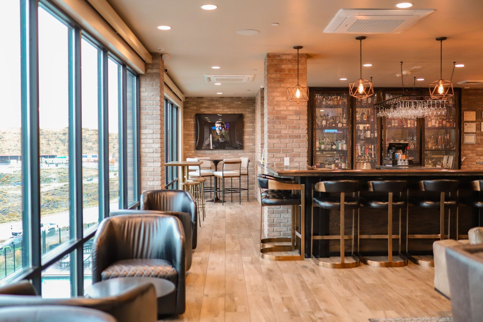 A bar area with a high ceiling, exposed brick walls, and a view through large windows.