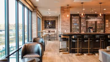 A bar area with a high ceiling, exposed brick walls, and a view through large windows.