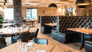 A restaurant interior with round tables, black leather booths, and pendant lighting.