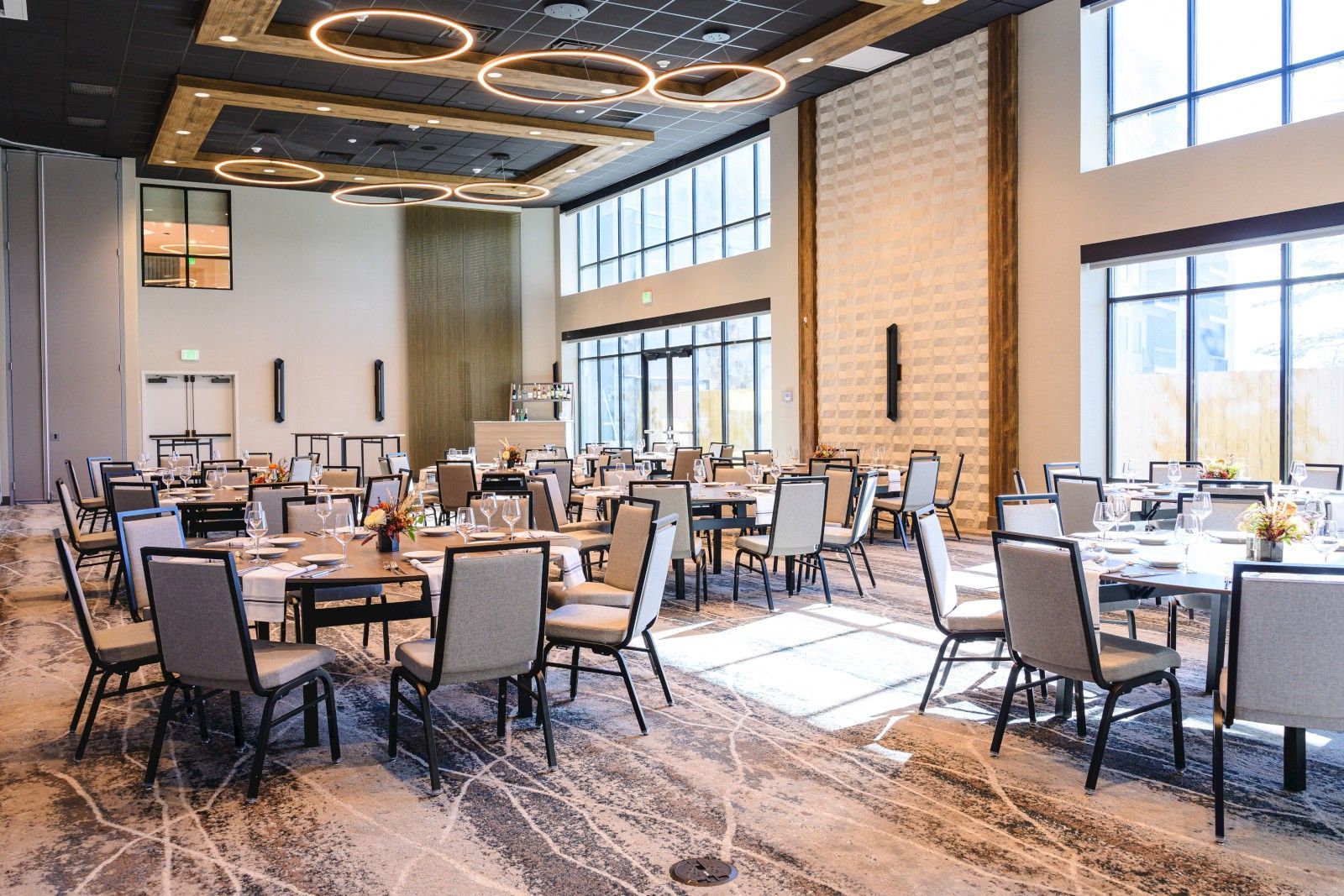 A spacious conference room with multiple tables and chairs, large windows, and a modern ceiling design.