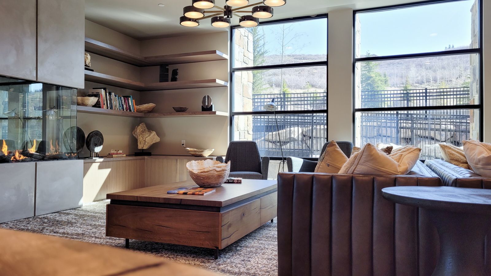 A modern living room with a fireplace, seating area, and large windows offering a view of the outdoors.