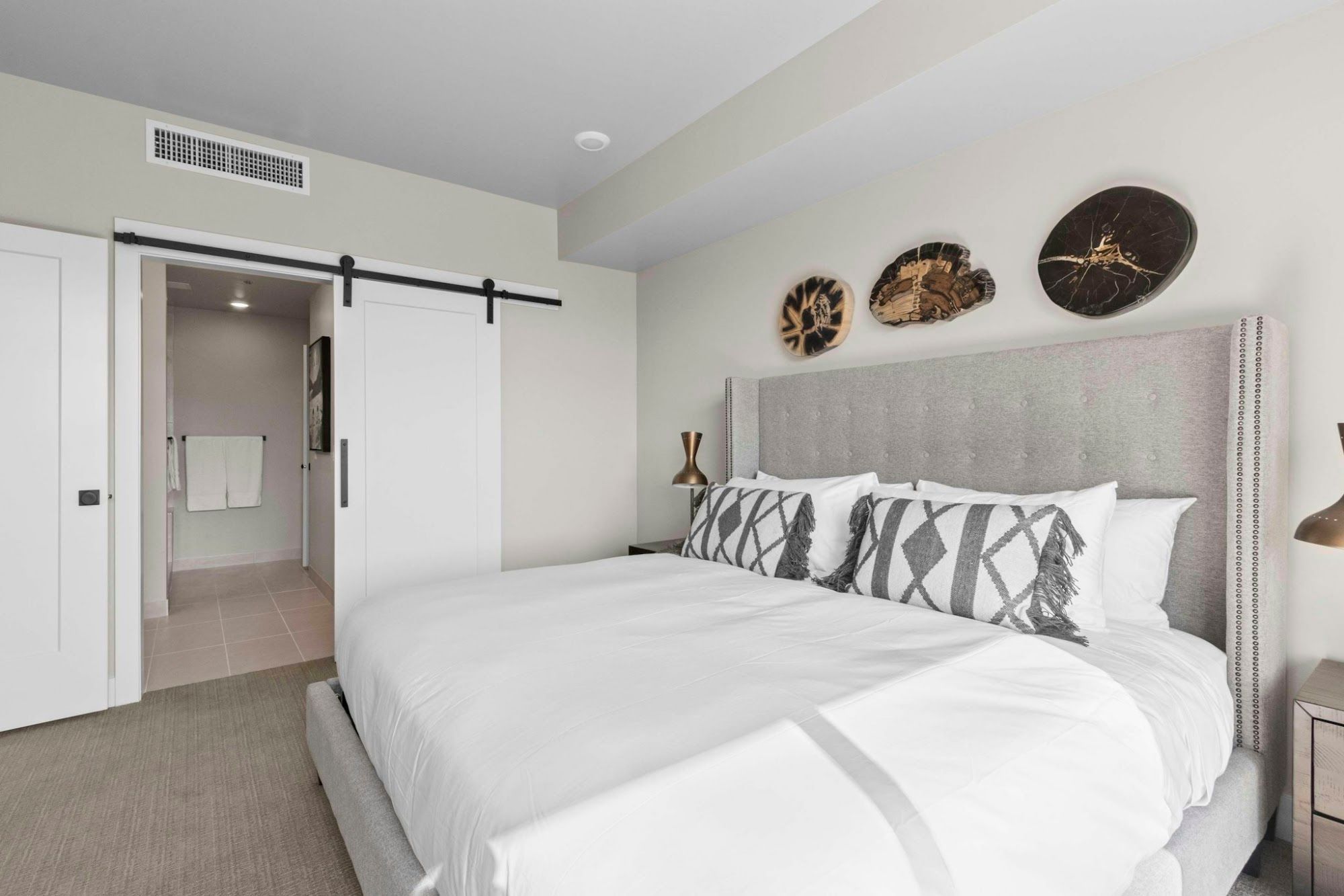 A bedroom with a large bed, a sliding door, a bedside table, and wall art.