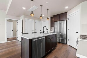 Cozinha moderna com ilha central, eletrodomésticos de aço inoxidável e iluminação pendente.