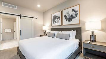 A hotel room with a bed, two bedside tables with lamps, a wardrobe, and two framed artworks on the wall.