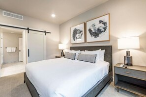 A hotel room with a bed, two bedside tables with lamps, a wardrobe, and two framed artworks on the wall.