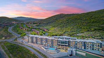 A multi-story hotel with a pool, surrounded by a hilly landscape.