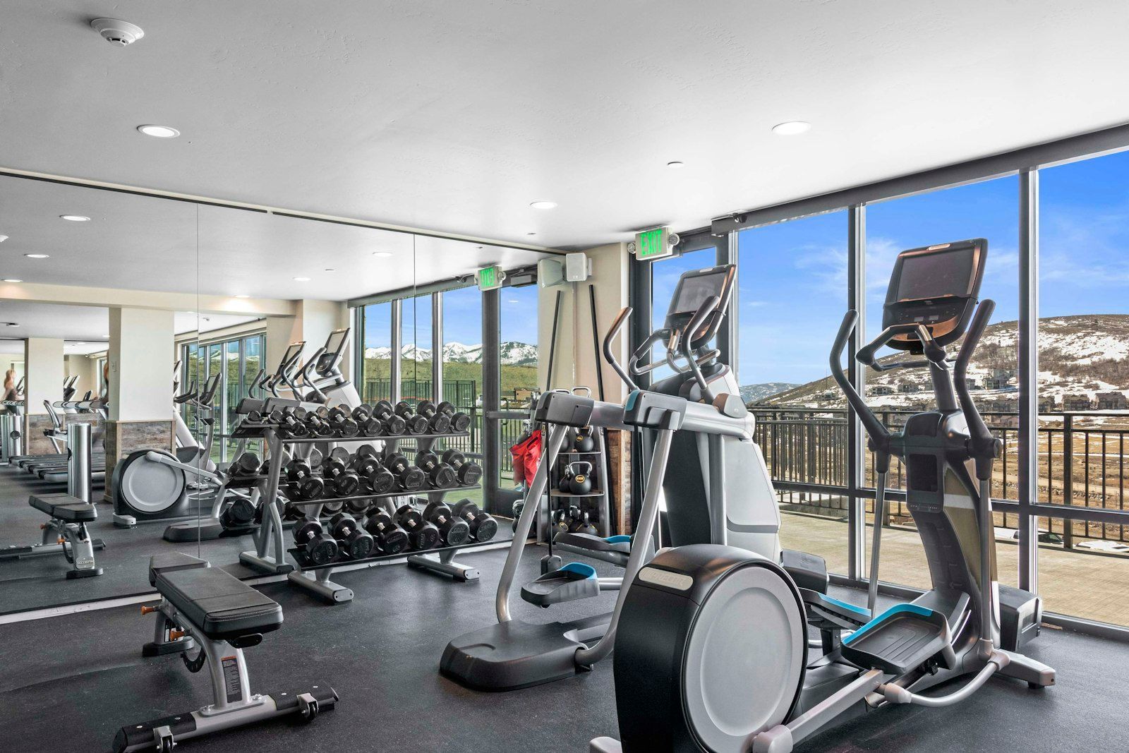 A gym with various exercise equipment, large windows, and a view of snow-capped mountains.