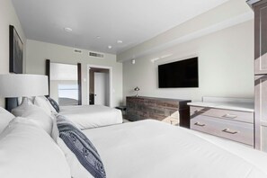 A hotel room with a bed, a dresser, a TV, and a door leading to another room.