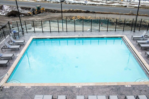 Une piscine rectangulaire bordée de carreaux, entourée de chaises longues et d’une clôture en métal.