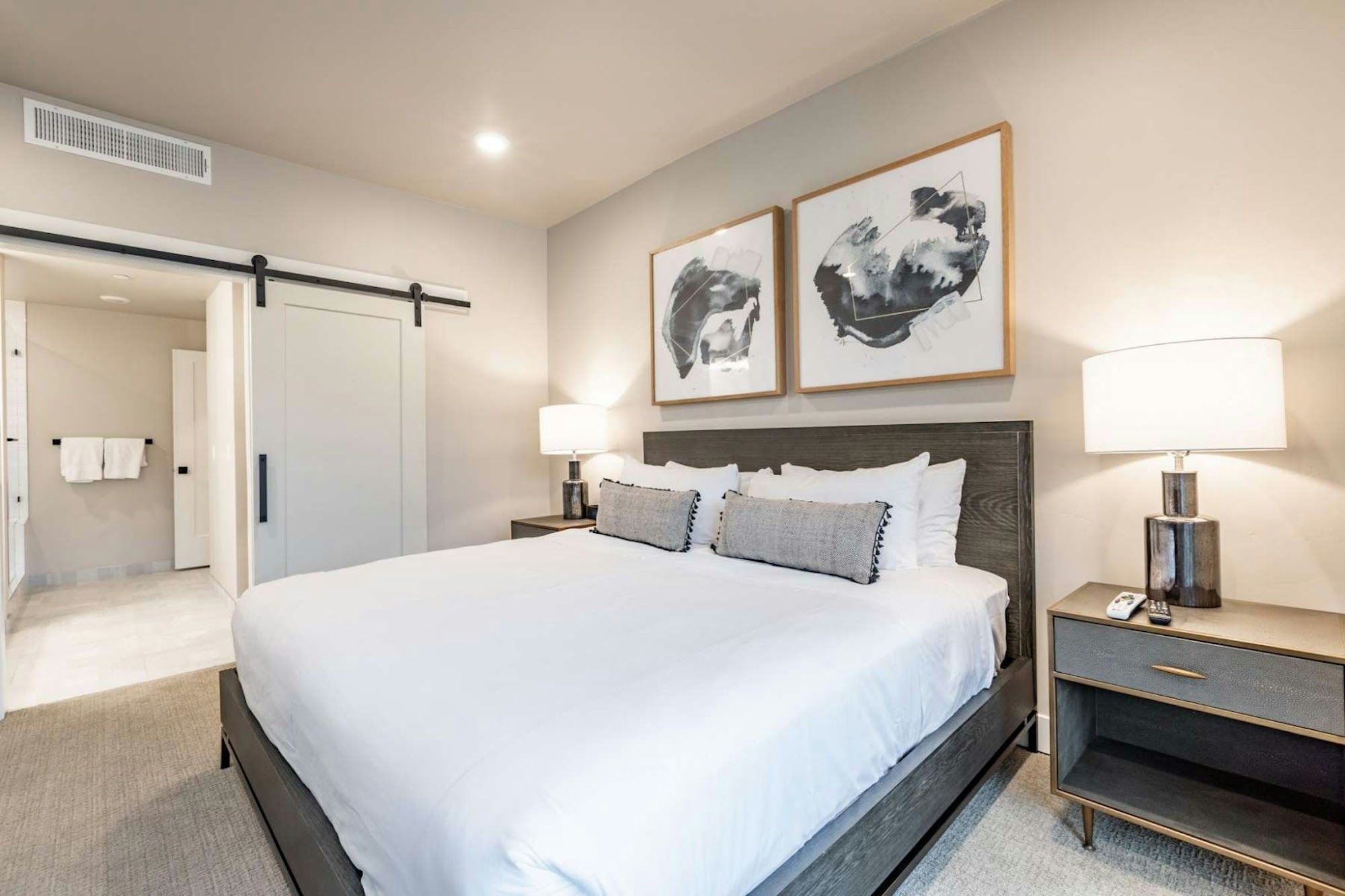 Een hotelkamer met een bed, twee nachtkastjes met lampen, een kledingkast, en twee kunstwerken in lijsten aan de muur.