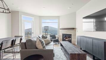 A modern living room with a fireplace, a dining area with a table and chairs, and large windows offering a view of the landscape.