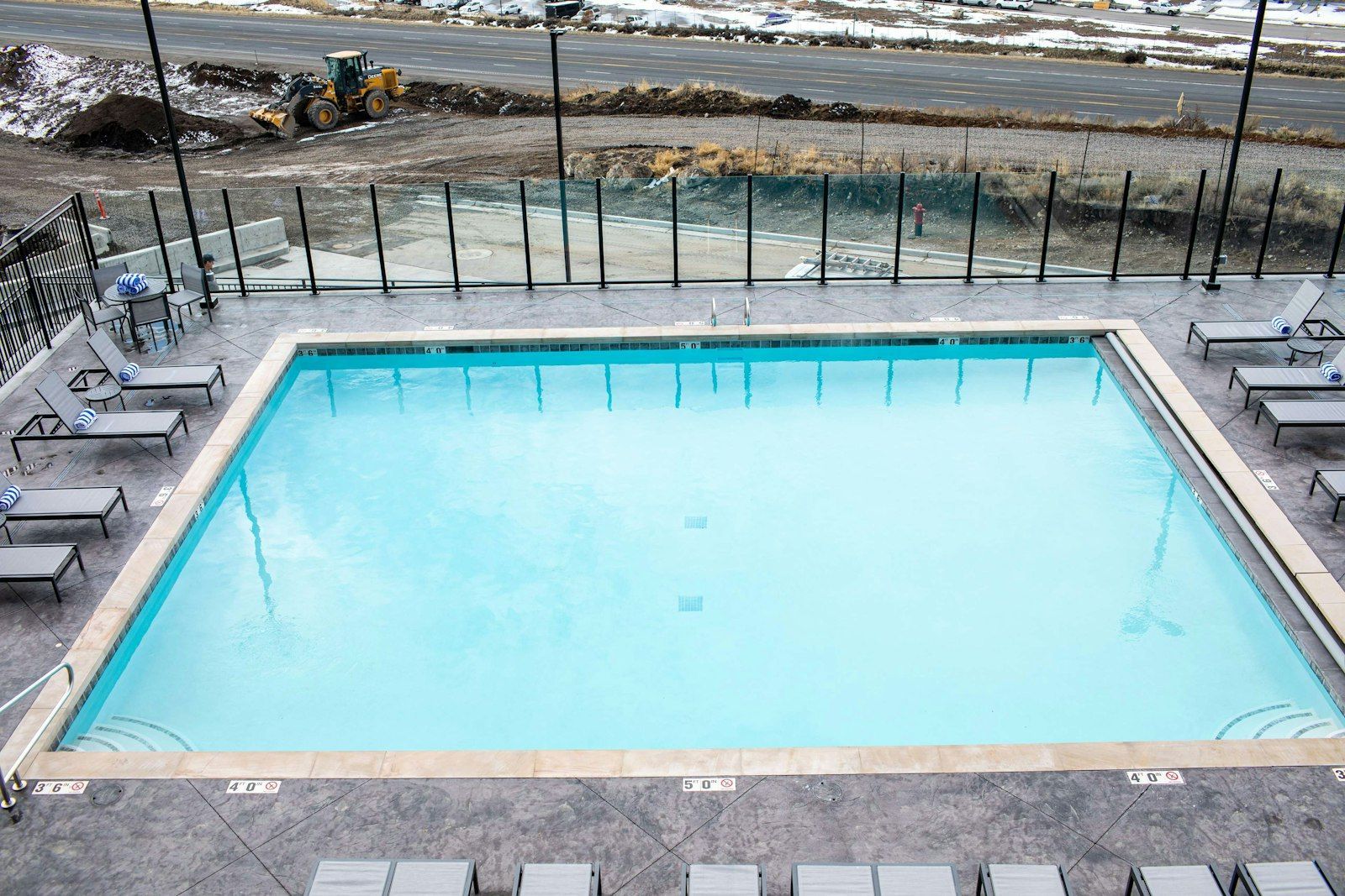 Una piscina rettangolare con bordo piastrellato, circondata da sdraio e una recinzione metallica.