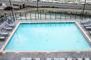 Piscina retangular com borda ladrilhada, rodeada por espreguiçadeiras e uma cerca de metal.