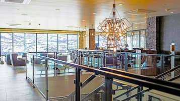 Eine geräumige Lobby mit einem modernen Kronleuchter, einer Sitzecke und Blick ins Freie.