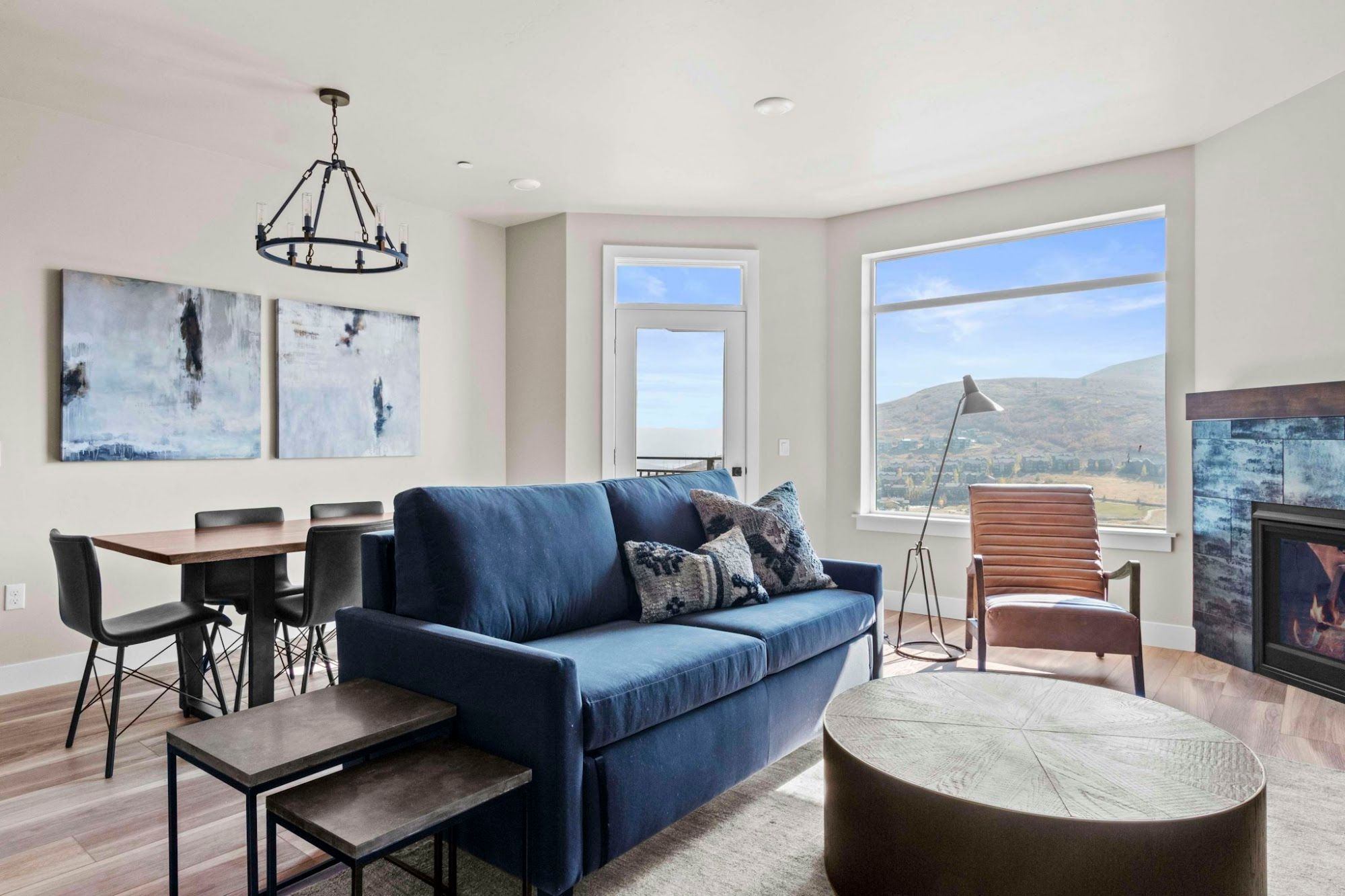 A modern living room with a blue sofa, a round coffee table, and a dining area with chairs and a table.