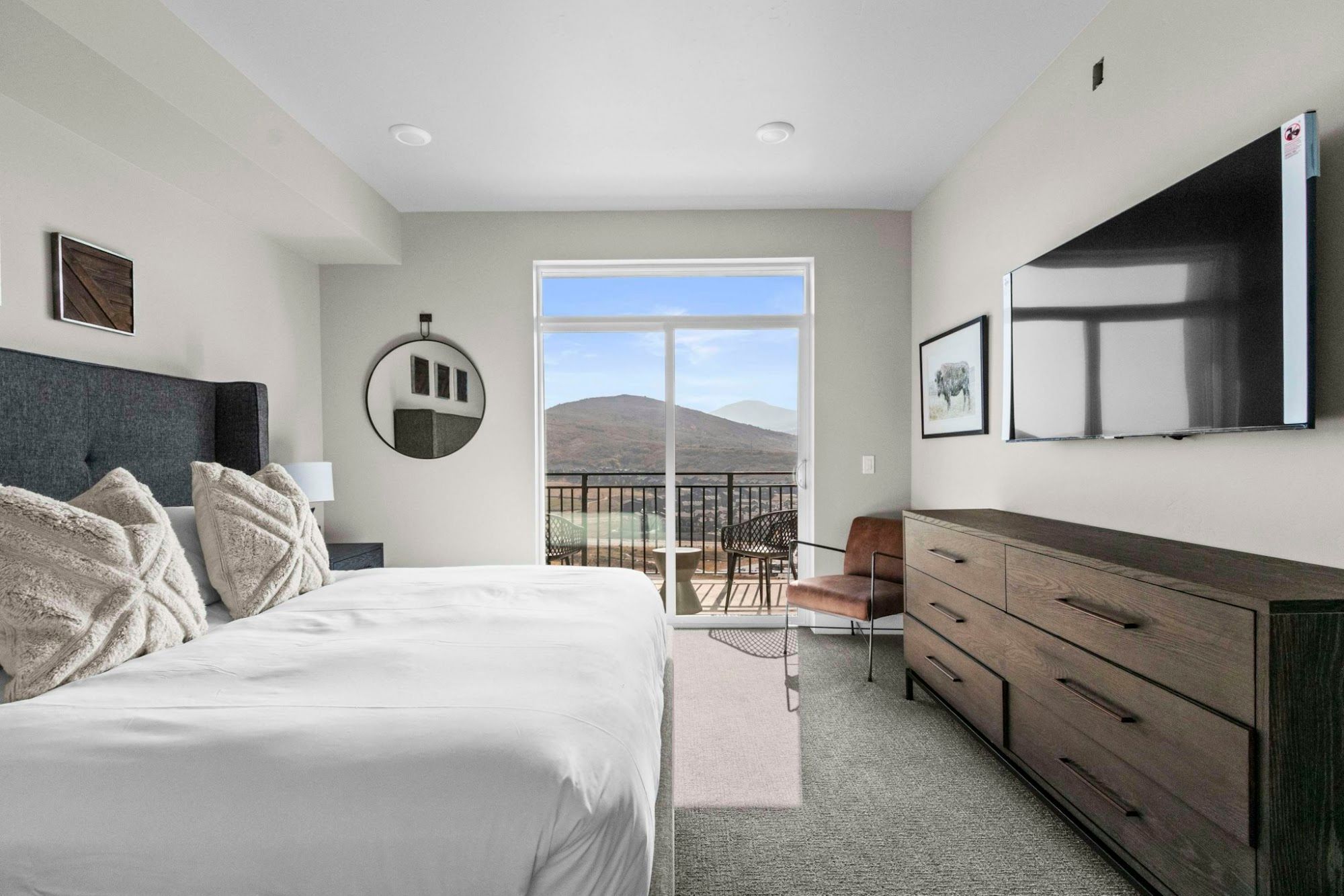 A bedroom with a bed, a dresser, a TV, and a balcony with a mountain view.