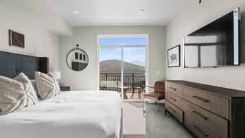 A bedroom with a bed, a dresser, a TV, and a balcony with a mountain view.