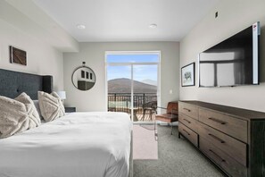 Quarto com cama, penteadeira, TV e varanda com vista para as montanhas.
