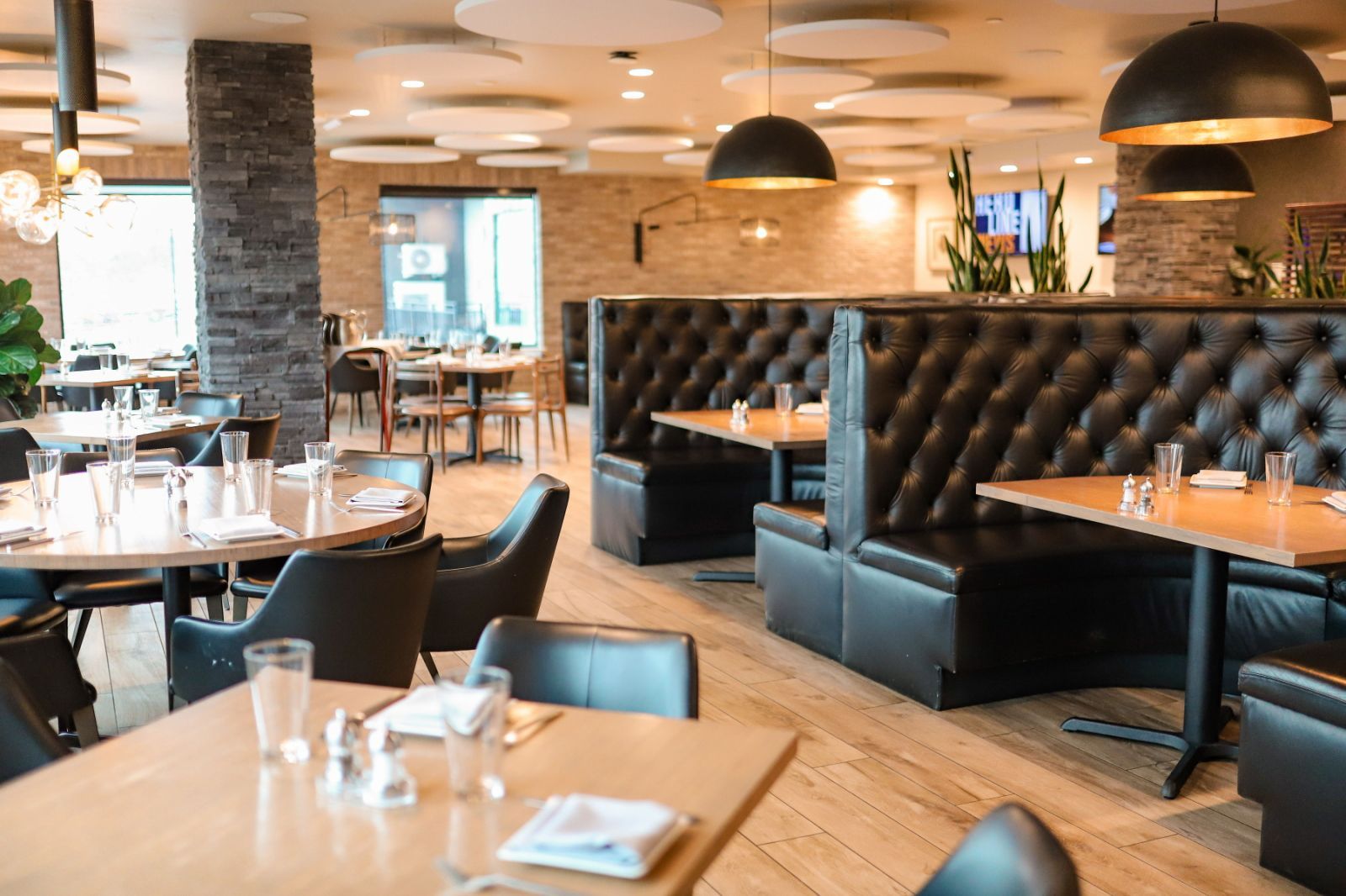 A restaurant interior with round tables, black leather booths, and pendant lighting.