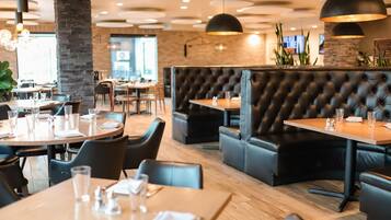 A restaurant interior with round tables, black leather booths, and pendant lighting.