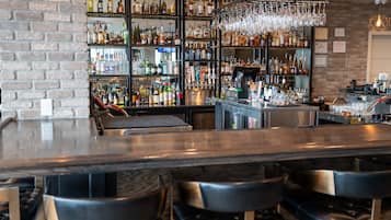 A bar area with a brick wall, shelves of liquor bottles, and black bar stools.