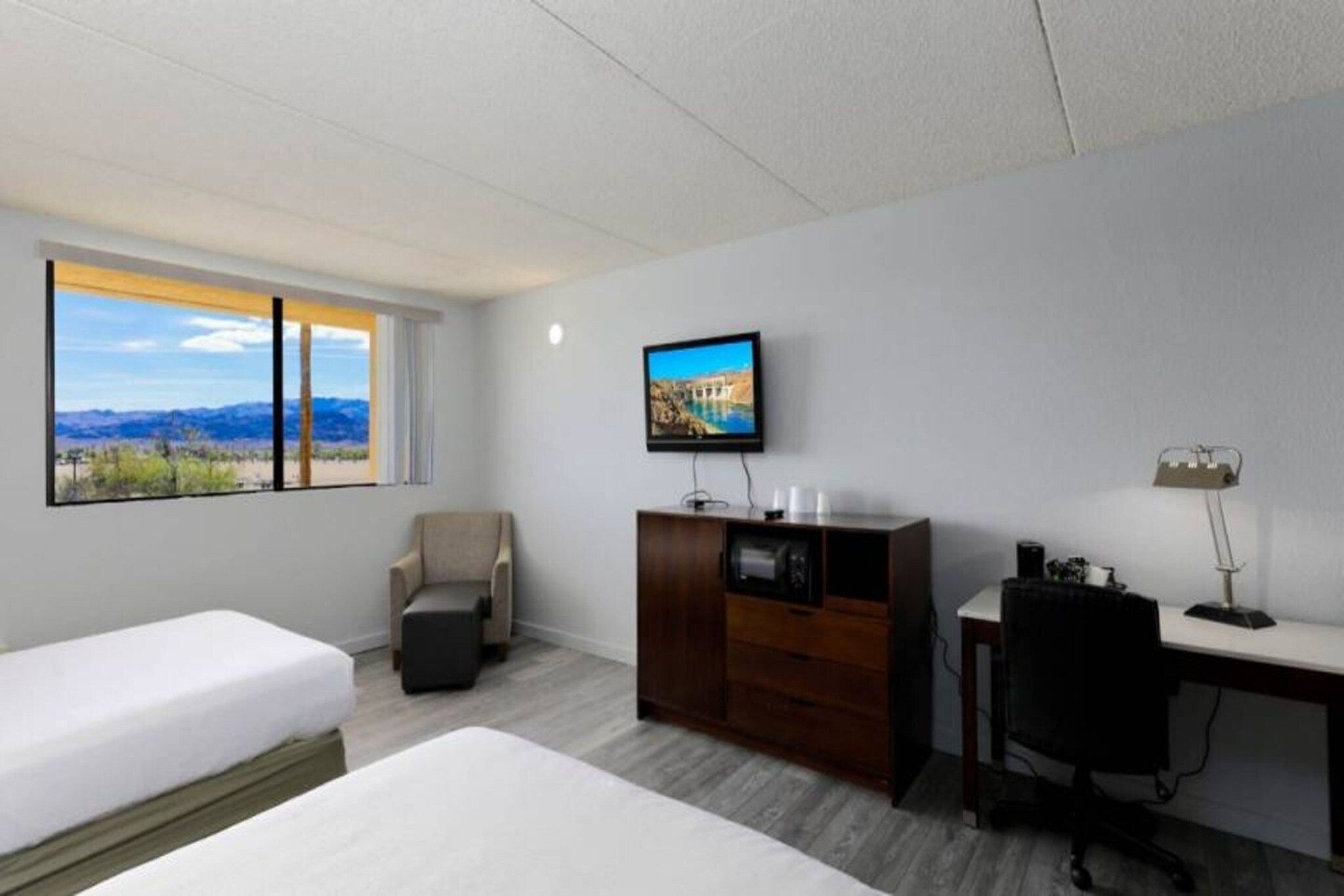 Une chambre d’hôtel équipée d’un lit, d’un bureau, d’une chaise, d’une télévision et d’une fenêtre donnant sur les montagnes.