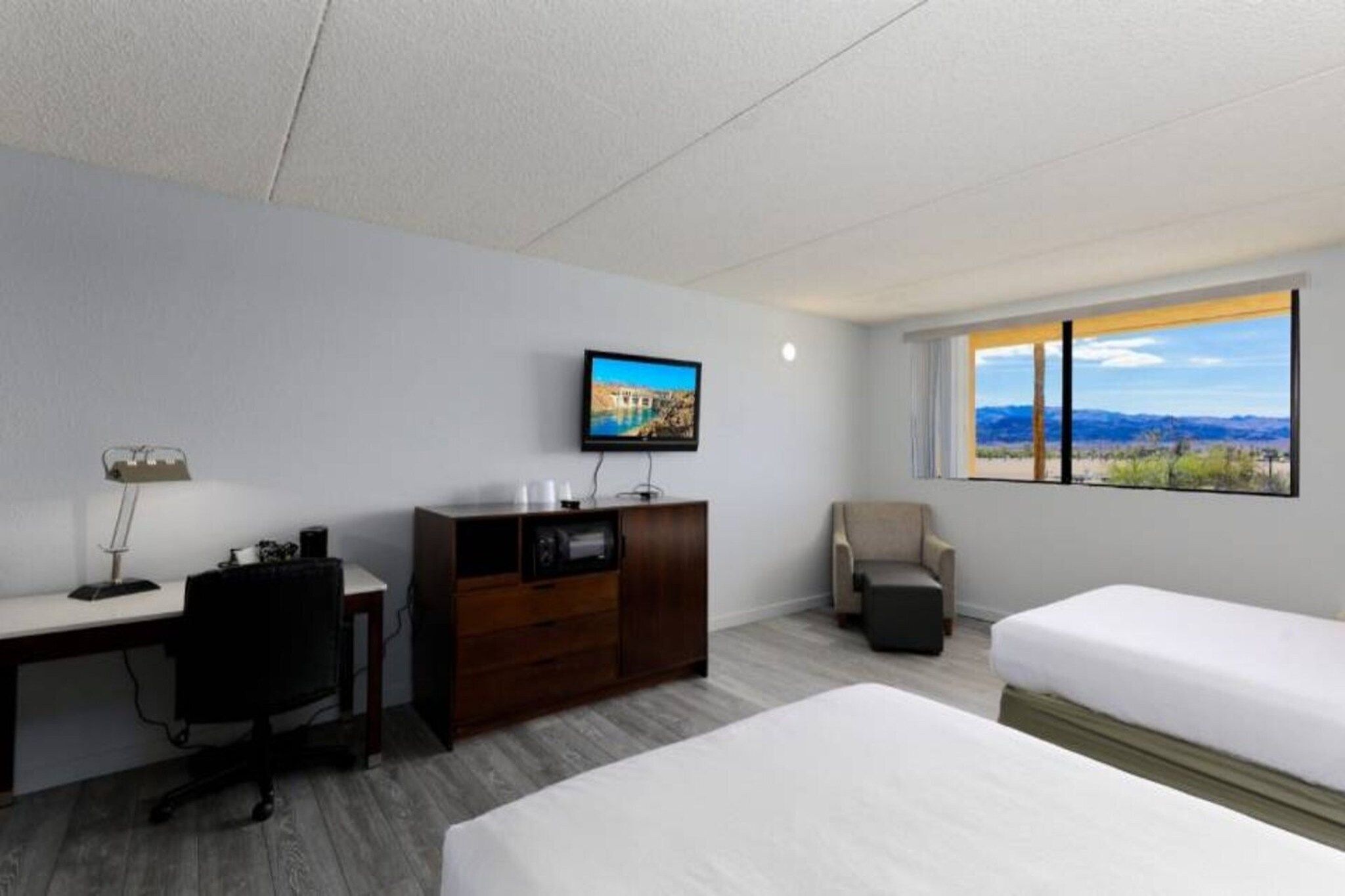 Een hotelkamer met een bed, een bureau, een stoel, een televisie en een raam met uitzicht.