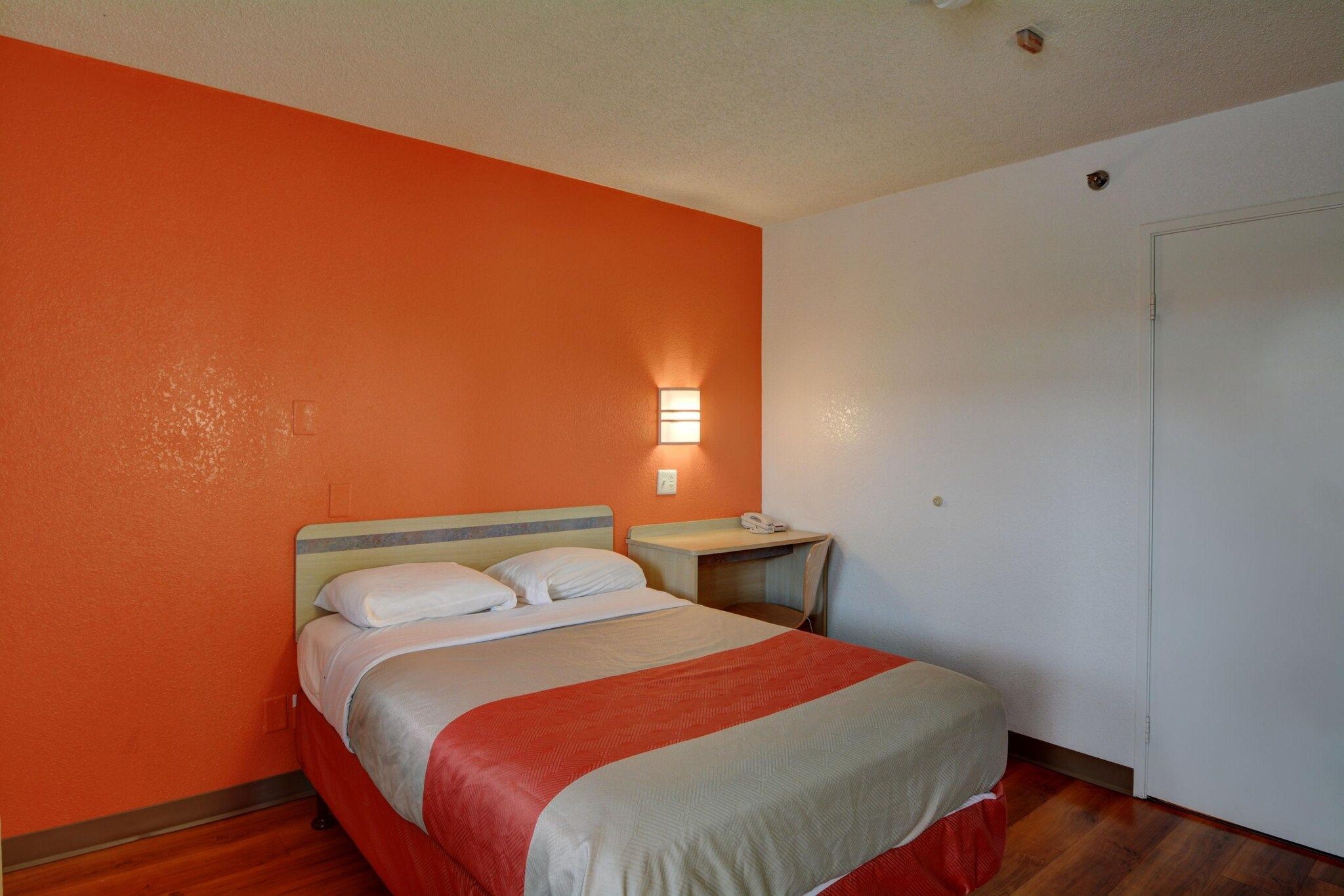 Habitació d'hotel amb llit, taula de nit i aplíc de paret.