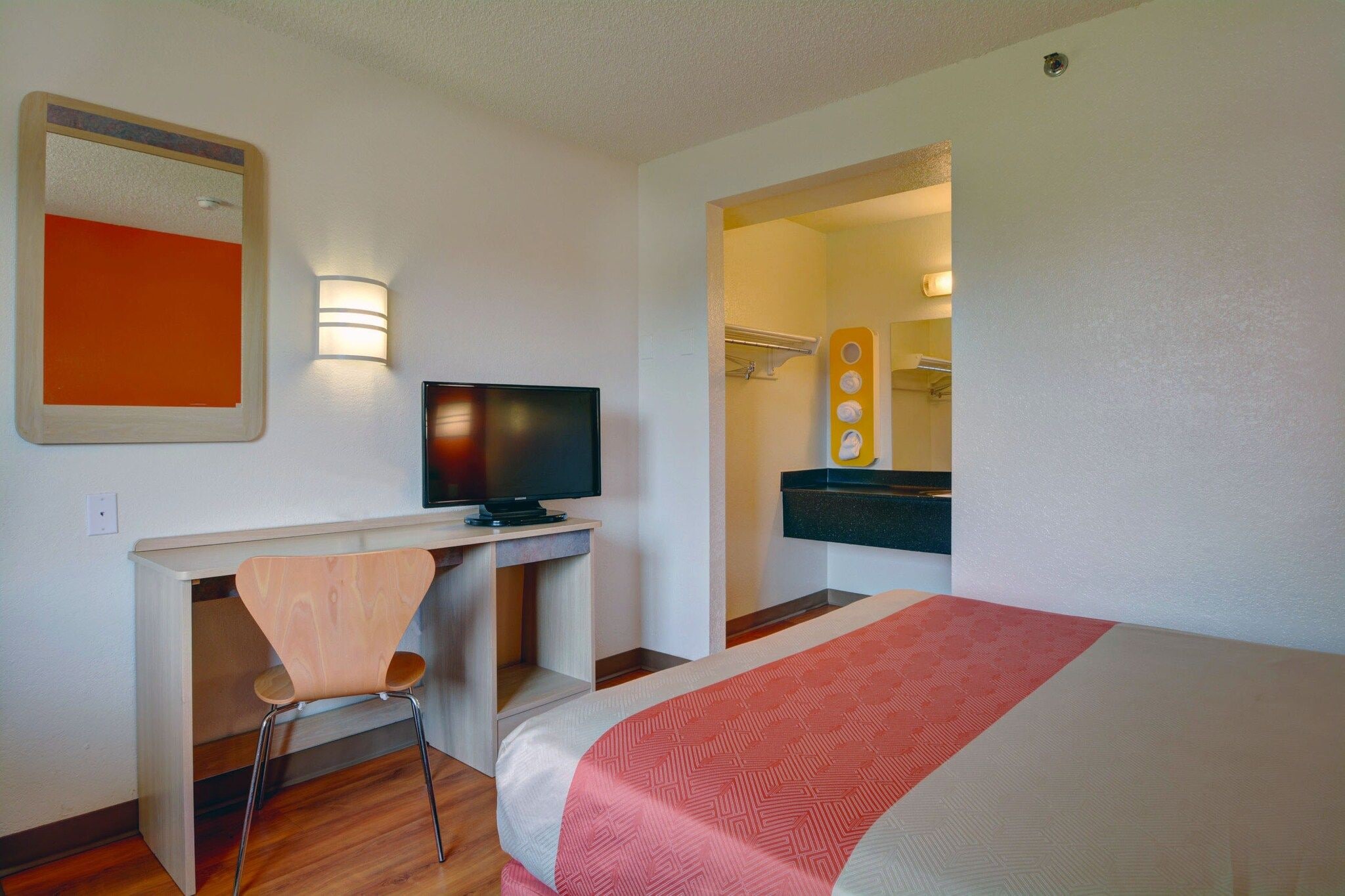 Une chambre d’hôtel avec un lit, un bureau et une chaise, un téléviseur et une salle de bain visible à travers une porte ouverte.