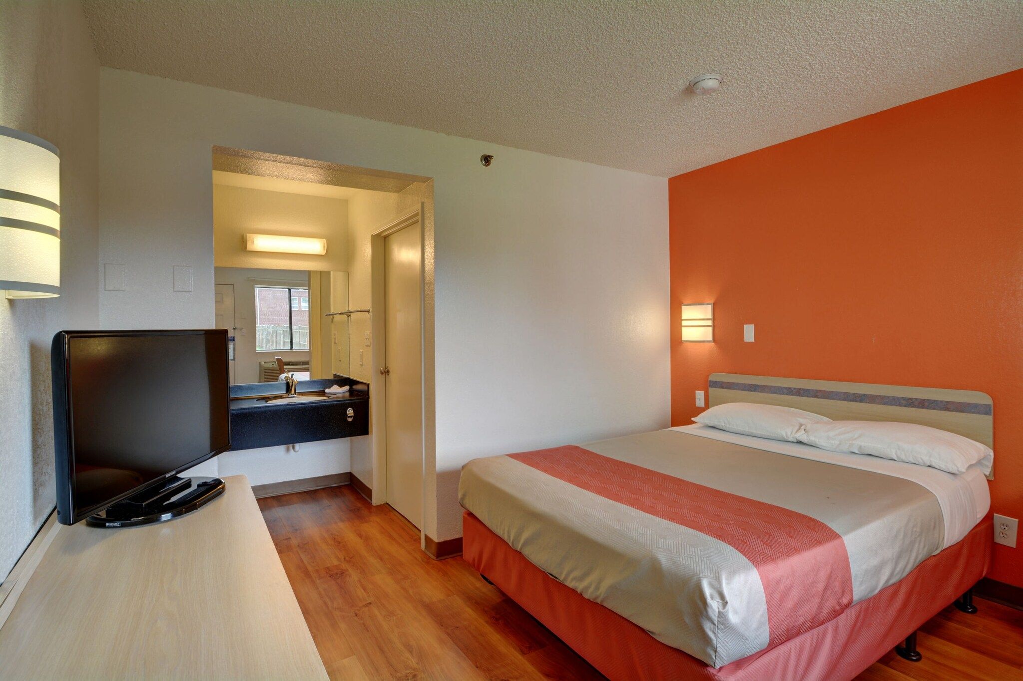 Une chambre d’hôtel avec un lit, un bureau avec une télévision et une salle de bain visible à travers une porte ouverte.