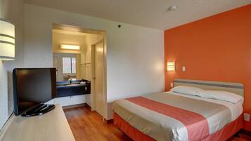 Une chambre d’hôtel avec un lit, un bureau avec une télévision et une salle de bain visible à travers une porte ouverte.