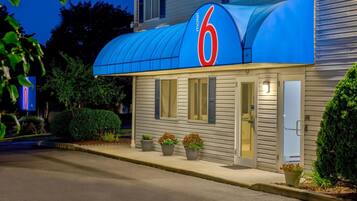 A motel with a prominent '6' sign, a covered entrance, and potted plants at the entrance.
