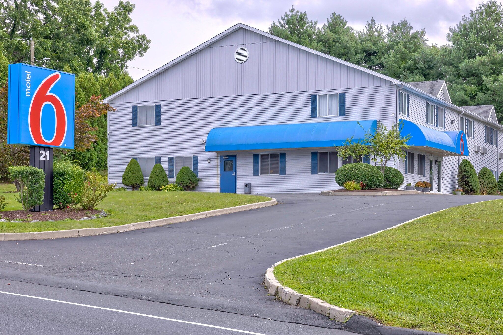 A motel with a large blue awning, a sign indicating it is number 6, and a well-maintained lawn.