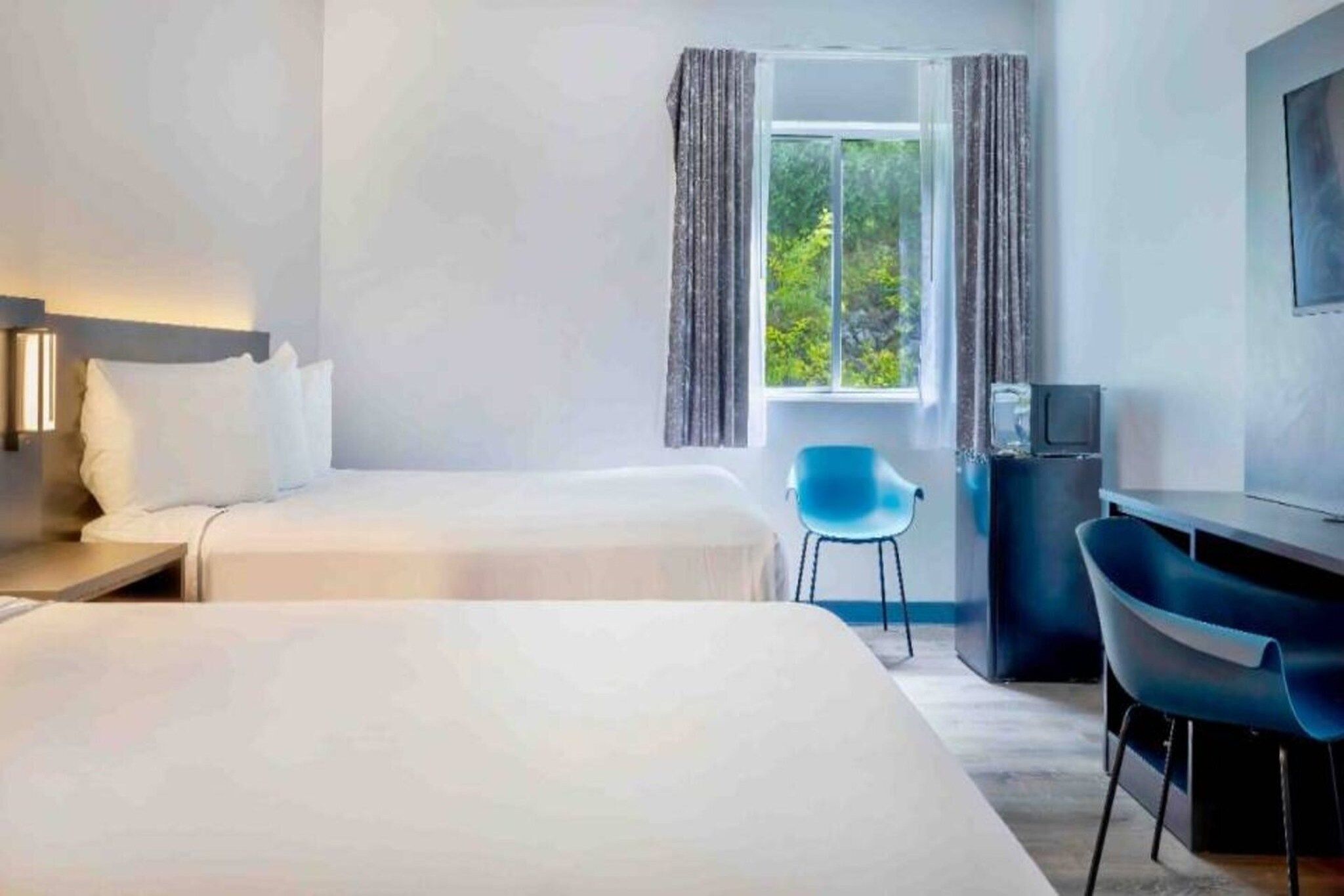 Habitación de hotel con dos camas, un escritorio, una silla y un televisor.